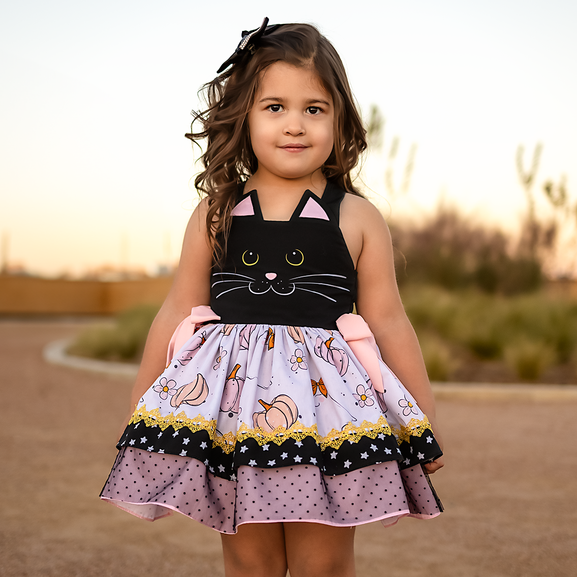 Young girl wearing a black cat dress with a patterned skirt outdoors. Halloween Dress.